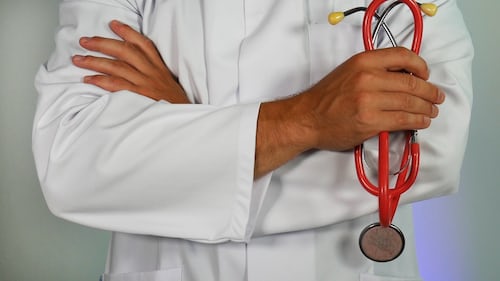 A doctor with folded arms in a white coat holding a stethoscope