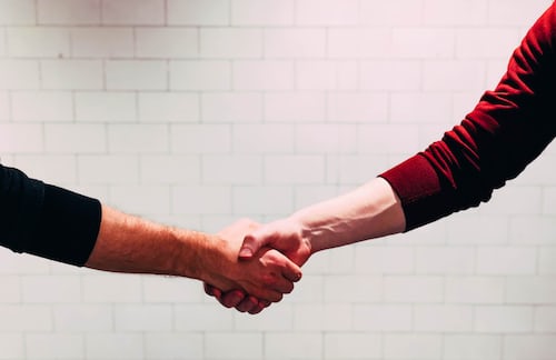 A handshake between two men with a white brick wall in the background