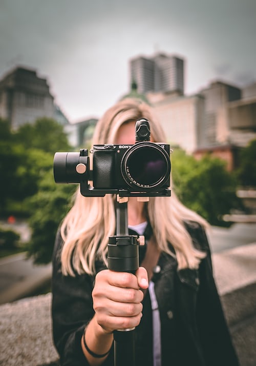 A lady holding a Lumix DSLR camera on a gimbal inn a city